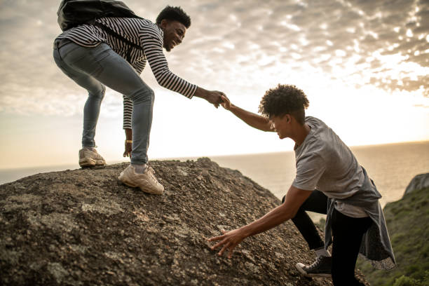 istock Young man helping his friend to climb up 1410132124