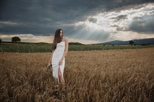 Beautiful young bride standing on a field in nature alone and holding a bouquet.