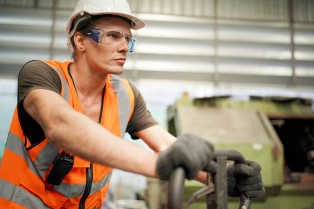 Young Caucasian hardworking heavy industry worker in protective suit and helmet using tablet and screwing valve.