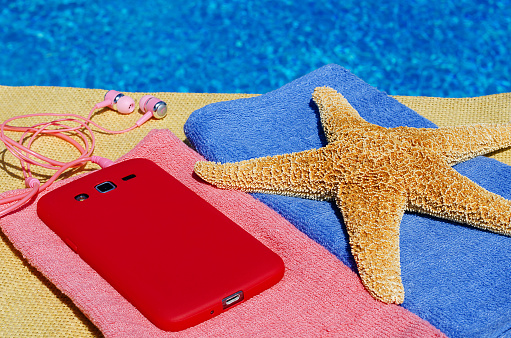 Starfish, mobile phone and headphones on bright towels against the backdrop of the pool. Relax outdoors next to the pool.