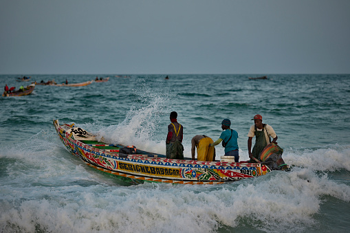 Nouakchott. Mauritania. October 03, 2021. Struggling with the waves of the surf, fishermen daily sail out on special wooden boats with a motor for several days in the open Atlantic Ocean for fishing.