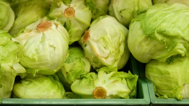 A heap of iceberg lettuce in trading baskets and a male buyer's hand takes one