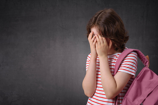 Portrait of a crying schoolgirl holding backpack, looking at camera