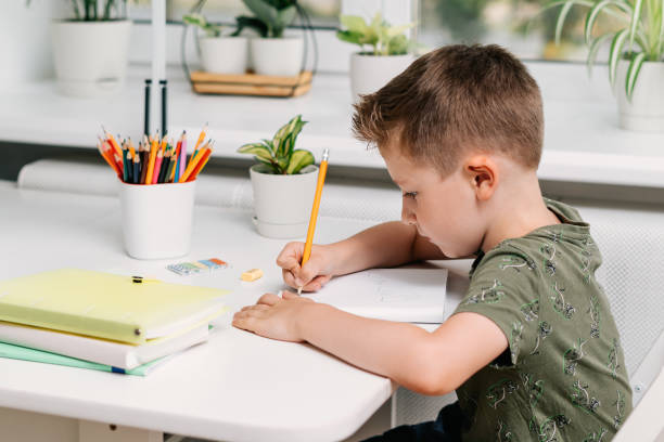 istock Back to school. Kid boy studying at home with book, writing in notepad and doing school homework. Thinking caucasian child siting at table with notebook. Distance learning online education 1410140389