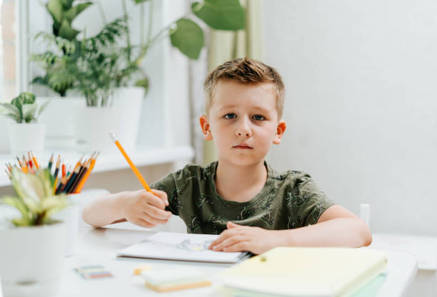 istock School kid boy studying at home with book, draw in notepad and doing homework. Thinking caucasian child siting at table with notebook. Back to school. Distance learning online education 1410140477