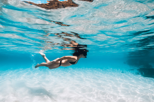 Woman in bikini and with diving mask swimming underwater in tropical transparent ocean with white sand bottom