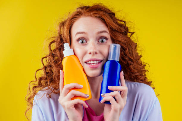 redhaired ginger curly woman holding sunscreen bottle making the right choice in studio yellow background stock photo