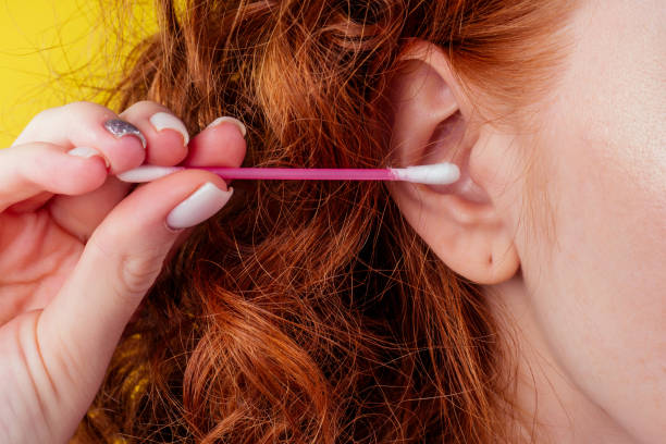 curly redhead caucasian woman use ears sticks in studio yellow background stock photo