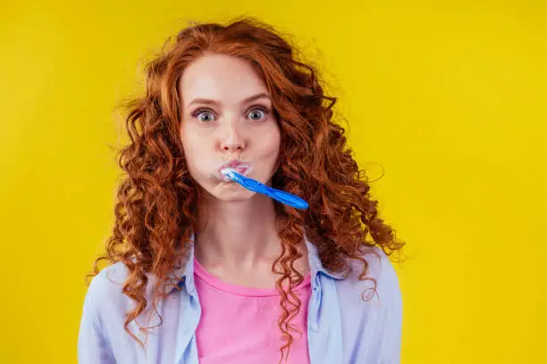 sleepy redhaired ginger woman brushing teeth with toothpaste eco paste on yellow studio background.