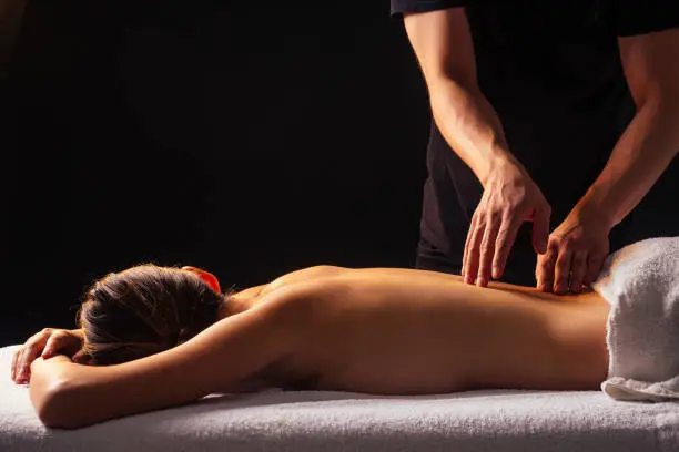 Masseur hands doing back massage to client in spa center in dark room.