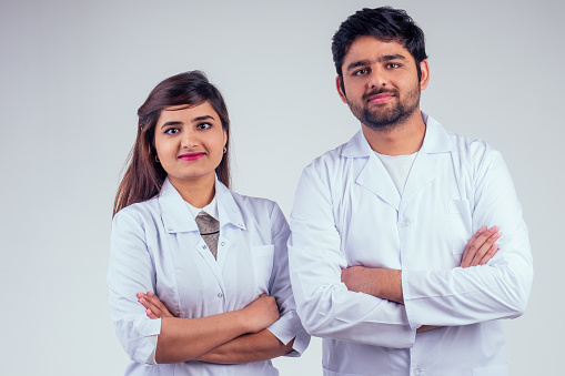 beautiful indian woman and handsome turkey man wearing white blazer coat arms crossed on the chest and looking at camera in studio background.