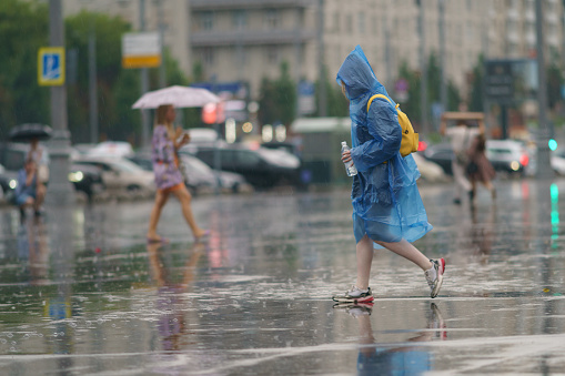 Moscow, Russia - July 10, 2022: Raining day in city at summer. Wet people. One woman hiding under umbrella. Other put on rain coat. Texture of strong, fresh and powerful water drops and sprays. Tropical storm.