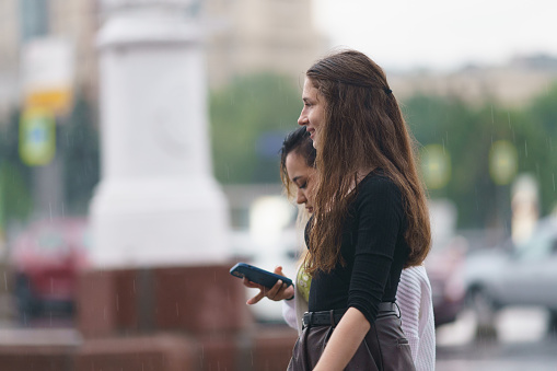 Moscow, Russia - July 10, 2022: Happy young women after the rain in city at summer. They are wet but are happy.