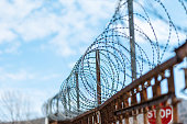 A metal fence with barbed wire under tension. Bright blue sky on the background. The concept of border protection, prison and military base