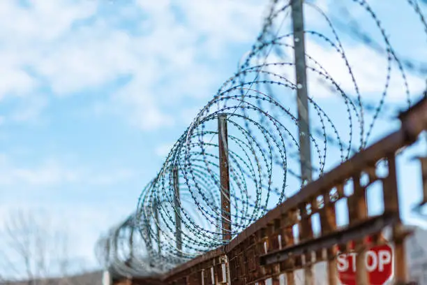 Photo of A metal fence with barbed wire under tension. Bright blue sky on the background. The concept of border protection, prison and military base