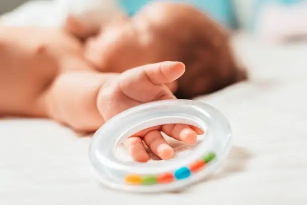 A baby is holding a rattle. Hand close-up, baby in blur.