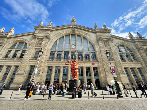 Paris, France -  10th June, 2022: People outside Gare du Nord railway station. The red Angel Bear statue in front of the entrance is by Richard Texier.