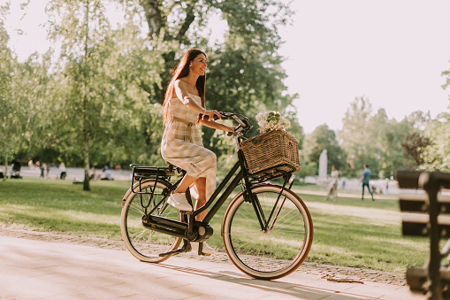 Pretty young woman riding  electric bike with flowers in the basket
