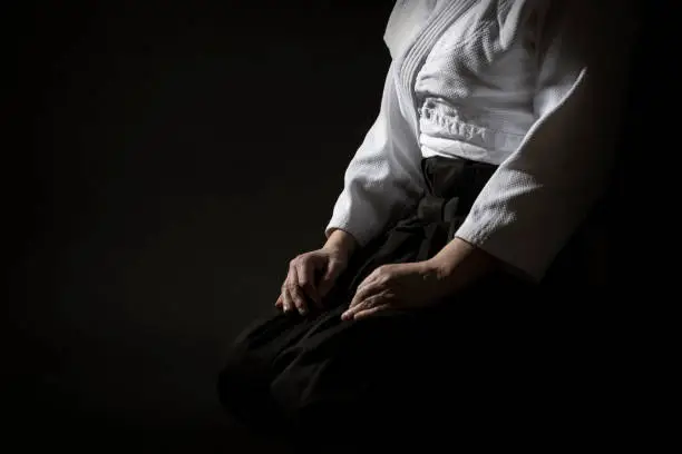 Aikido sitting pose in hakama uniform on black background. Shallow depth of field. SDF.