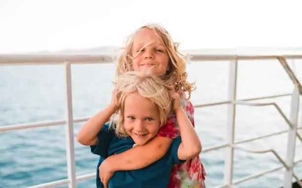 Front shot of adorable brothers spending vacation time together. Big brother puts arms around small brother while sailing in the sea.