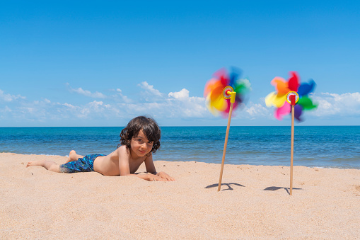 Sea, beach and colorful weather vane background.
boy lying on beach looking at camera. Taken with a full-frame camera in windy and sunny weather.