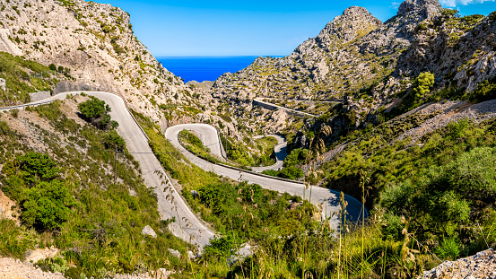 Mallorca winding road MA-2141 leading through extreme terrain in a valley of Serra de Tramuntana mountains, curving in tight serpentines down to village Sa Calobra with view to the mediterranean sea.