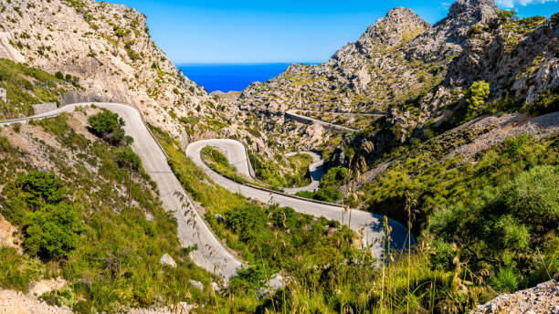 View to the mediterranean sea down the narrow Serra de Tramuntana pass road MA-2141 winding in serpentines down to tourist attraction Sa Calobra at Mallorca below the famous place Nus de sa Corbata. Mallorca winding road MA-2141 leading through extreme terrain in a valley of Serra de Tramuntana mountains, curving in tight serpentines down to village Sa Calobra with view to the mediterranean sea. kruis stock pictures, royalty-free photos & images