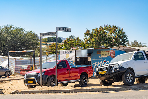 Corner of Clemence Kapuuo and Exodus Street at Katutura Township near Windhoek at Khomas Region, Namibia, with commercial signs and cars in the background. Clemence Kapuuo (1923-1978) was a politician and chief of the Herero people.