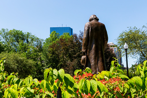 Boston, Massachusetts, USA - July 19, 2022: Rear view of the bronze statue of Edward Everett Hale in the Boston Public Garden, looking towards the Back Bay and the John Hancock Tower. Selective focus.