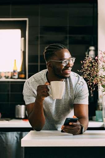 Young Afro-American man drinking his morning coffee, while reading news on his smartphone.