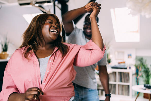 Couple Dancing At Home Cute young Afro-American couple having fun together at home, dancing and laughing. body positive couple stock pictures, royalty-free photos & images
