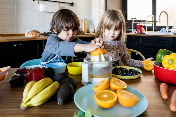 Twin siblings preparing fresh orange juice to surprise their mother. Twin siblings preparing fresh orange juice to surprise their mother. Sitting in the kitchen at home preparing a healthy breakfast, fresh fruits and vegetables on the counter. spanish breakfast stock pictures, royalty-free photos & images