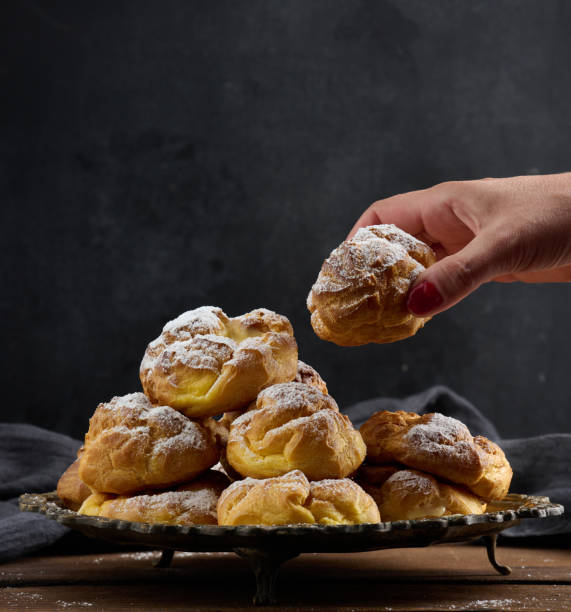 istock Baked eclairs with custard cream on a metal round plate sprinkled with powdered sugar 1410164277