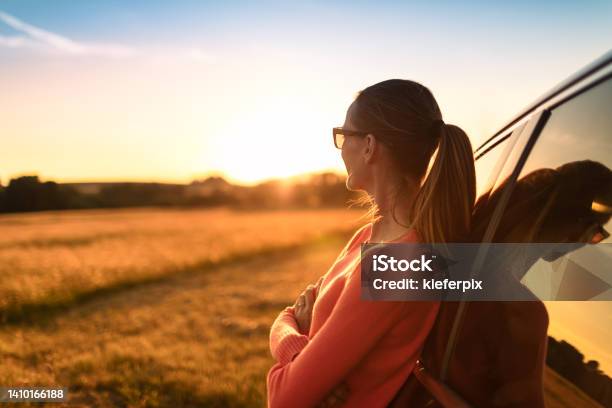 Thoughtful Female Traveler Relaxing Next To Car Looking Out At The Beautiful Golden Sunset View Stock Photo - Download Image Now