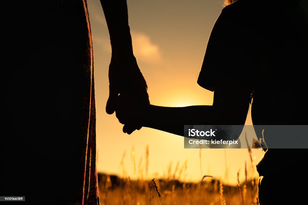 Silhouette of mother and child holding hands facing the sunset. Parenting and family lifestyle concept. Refugee Stock Photo