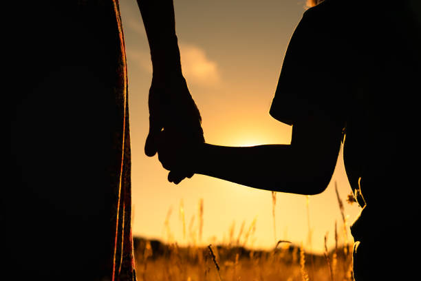 Silhouette of mother and child holding hands facing the sunset. stock photo
