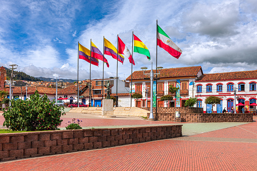 Zipaquira, Colombia - Looking across Independence Square in the Andean city of Zipaquirá, in the South American country of Colombia towards the Andean country flags on one side of the town square. The town is located on the Eastern Range of the Andes Mountains, at an altitude of 8,690 feet above mean sea level. The present day city was established in the year 1600 AD. Spanish colonial architecture and it's influence can be seen in the image. Photo shot in the afternoon sunlight; horizontal format.