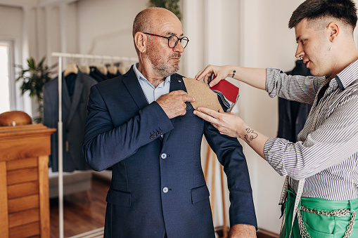 Male tailor showing a various types of textile materials to a mature male client for a new suit.