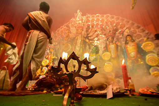 Howrah, West Bengal, India - 13th October 2021 : Goddess Durga is being worshipped by Hindu priests with holy panchapradip, in forground, during ashtami puja with holy smoke inside puja pandal.