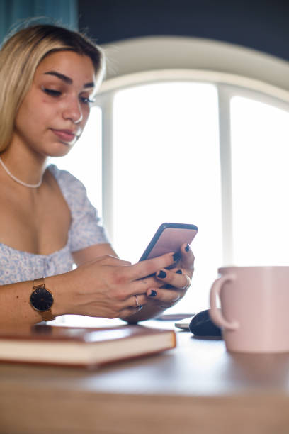 istock Low angle view of young woman texting via smart phone while working at her desk 1410194460