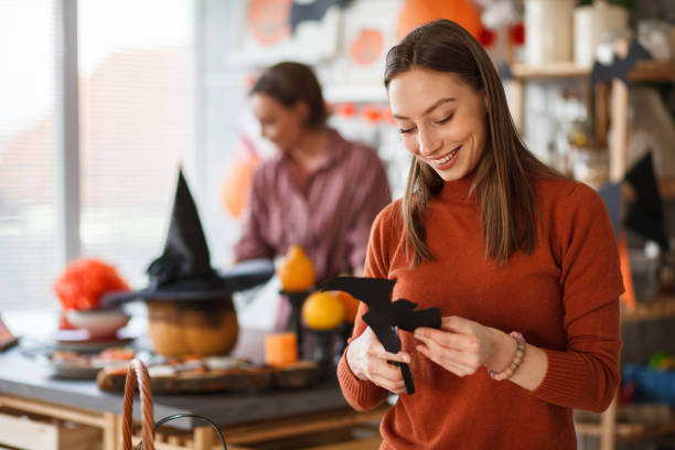 Young joyful woman cutting out a paper bat when making Halloween decorations