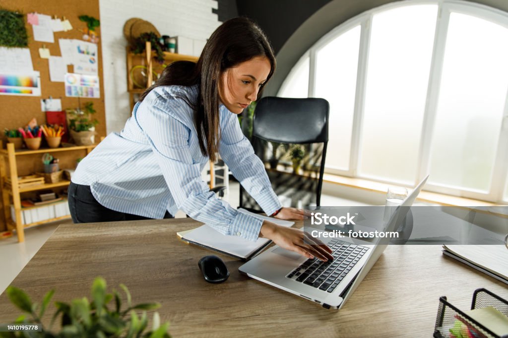 Young businesswoman standing over her desk, checking something on laptop quickly Copy space shot of focused young businesswoman standing over her desk, checking something on laptop quickly before she leaves to go home. Log Out Stock Photo