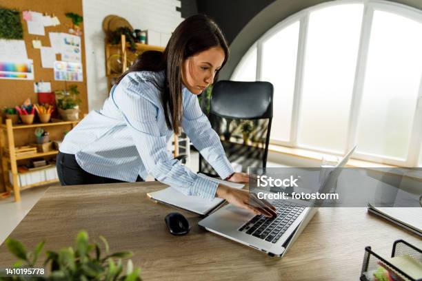 Young Businesswoman Standing Over Her Desk Checking Something On Laptop Quickly Stock Photo - Download Image Now