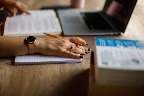 Close up shot of unrecognizable female student holding a pencil and resting her hand on a notebook while studying.