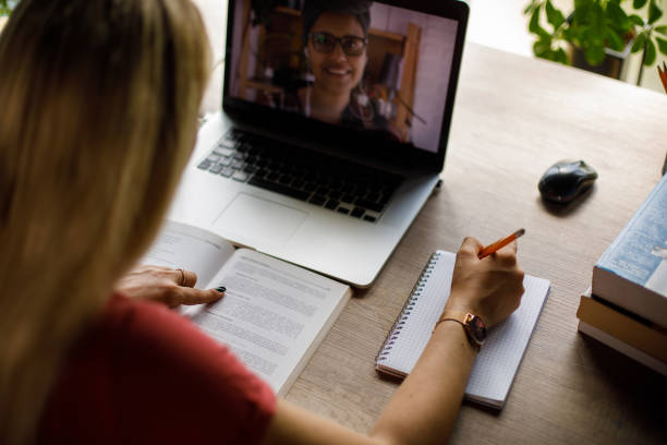 istock Young woman writing notes while attending online class via video call 1410196999
