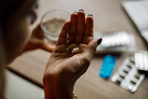 Close up shot of unrecognizable young woman holding various pills in the palm of her hand, that she is about to take.