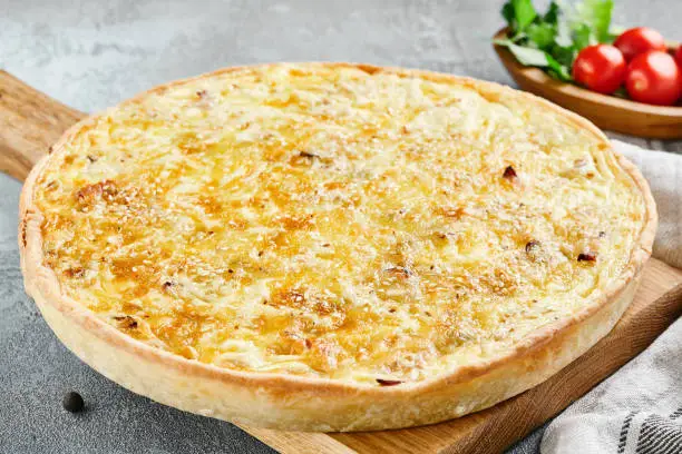 Open pie with mushrooms and cheese. Quiche lorraine  with cheese and sesame on gray stone background. French pie kish rustic style on stone table. Aesthetic composition with quiche on wooden board