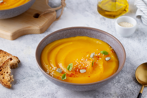 Pumpkin puree soup, served in a wide plate, garnished with seeds and herbs, vegetable dish