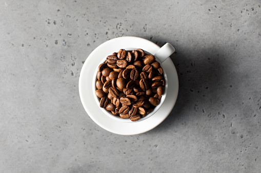 Roasted coffee beans in a white mug on a grey background. Copy space