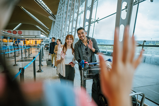 Welcome back, mom and dad. Happy young Asian Chinese girl waving hand greeting her mom and dad at arrival hall in airport,